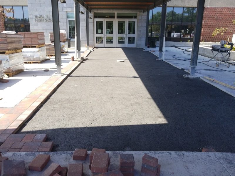 Compacted base course and brick paver edge banding being laid at the Roslyn High School entrance, with paver pallets staged alongside