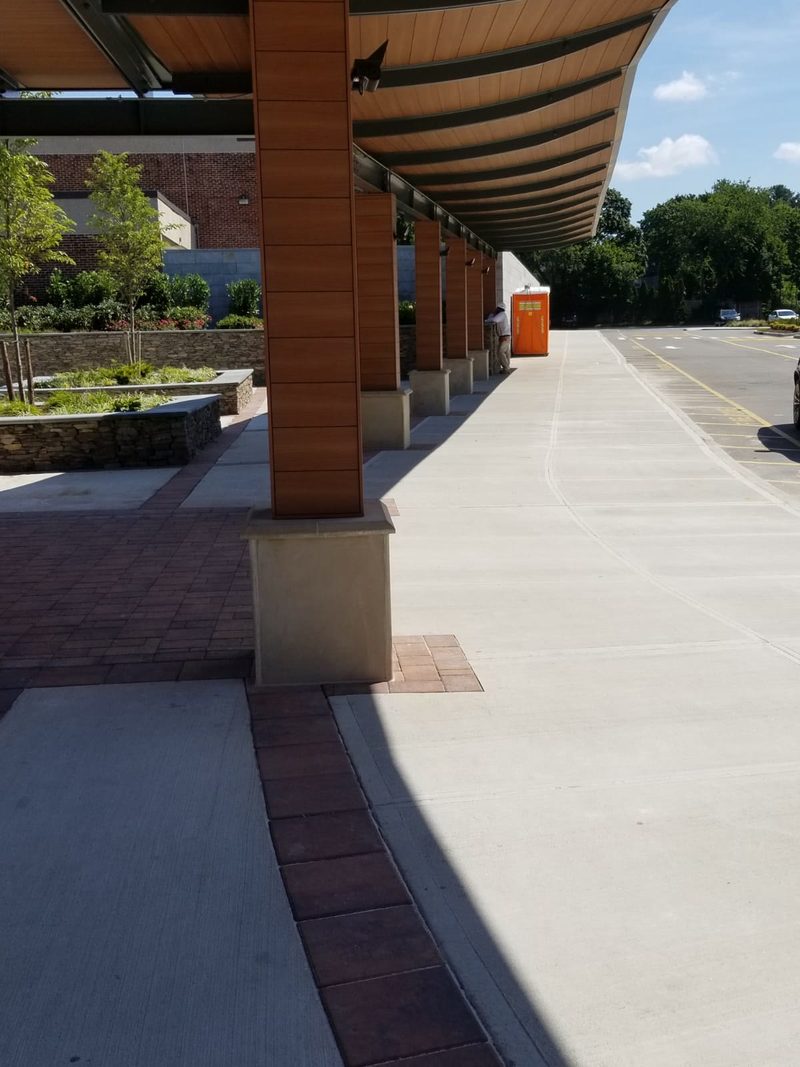 Completed concrete drop-off lane with brick paver banding, stone veneer planters and canopy at Roslyn High School