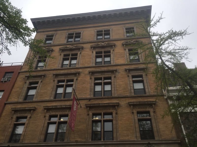 Buff brick institutional building facade with heavy limestone cornice, carved pediments and restored window surrounds